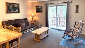 A cozy living room with a sofa, wooden table, rocking chair, and a view through a sliding glass door. - Mountain and River Views, Seasonal Pool, Near National Park (Estes Park)