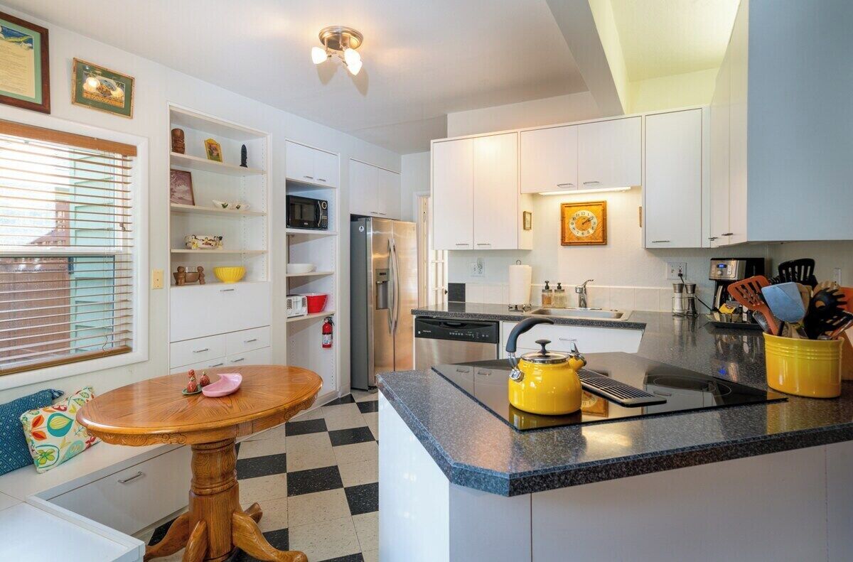 A modern kitchen with white cabinets, a central island, a microwave, and a refrigerator.