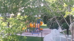 A playground with a slide and climbing structures, surrounded by trees and a white fence. - Upscale all the Way! 2BR 2BA Las Palmas Condo in St. George UT (St George)