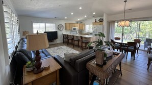 A spacious living area with a sofa, a coffee table, and a dining table with chairs. There is a kitchen in the background with wooden cabinets and a refrigerator. - Upscale all the Way! 2BR 2BA Las Palmas Condo in St. George UT (St George)