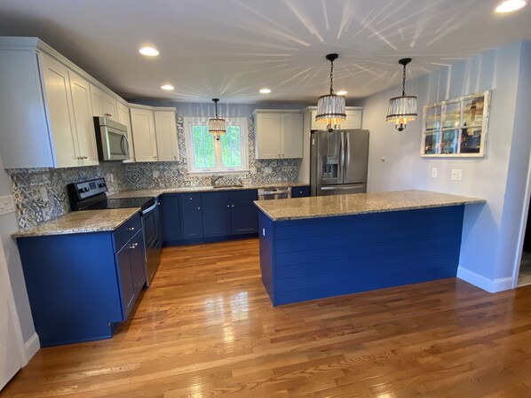 A modern kitchen with dark blue cabinets, granite countertops, stainless steel appliances, and pendant lighting.