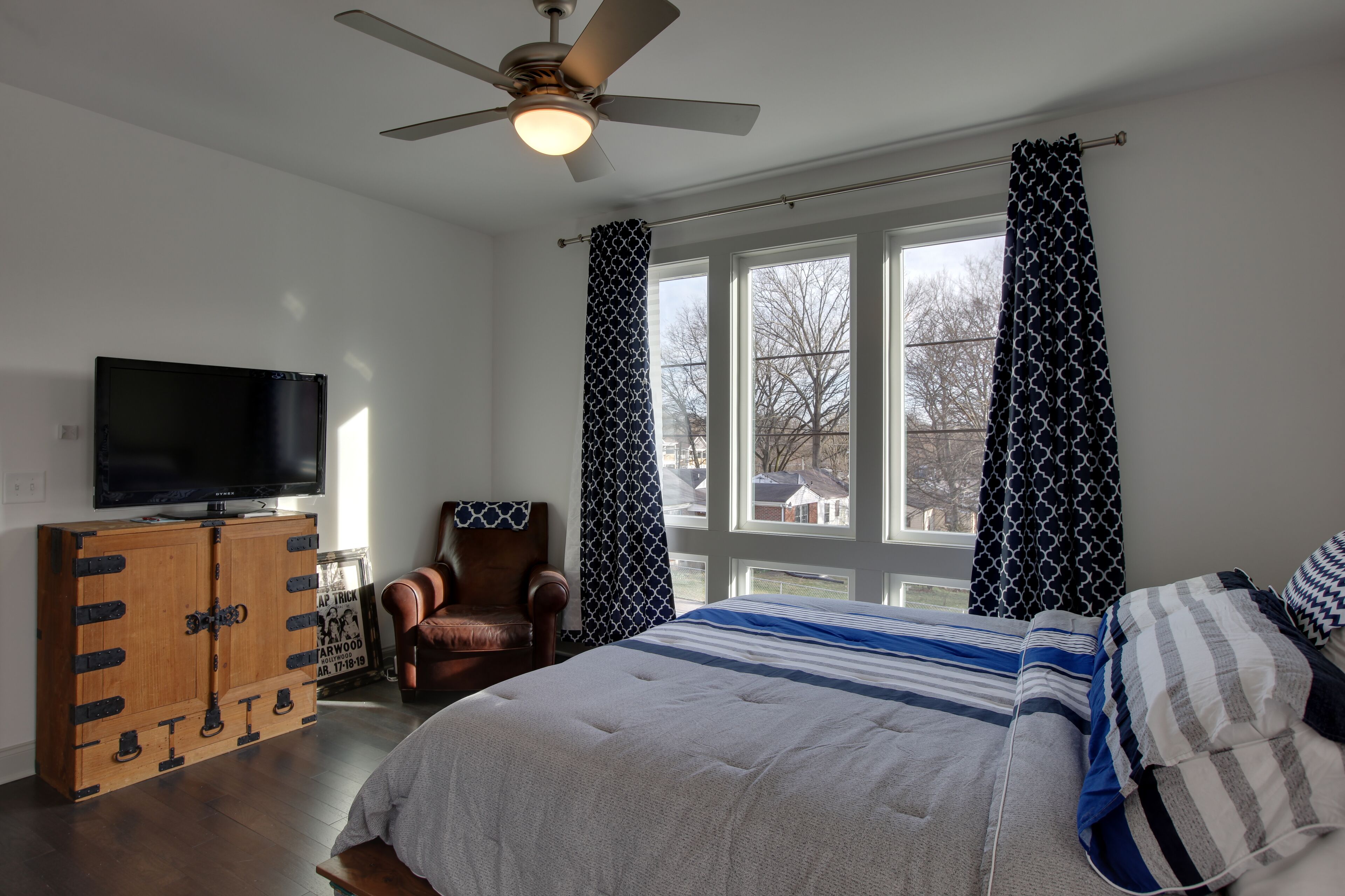 Une chambre à coucher comprenant un lit, un téléviseur, une armoire en bois, une chaise et une fenêtre avec des rideaux.