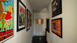 A hallway with framed posters on the walls, a dark wooden floor, and a white ceiling with a light fixture. - Music Centric Home, 5 minutes to Broadway. (Nashville)