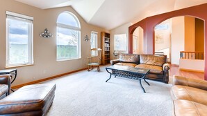 A spacious living room with a high ceiling, large windows, a leather sofa, a coffee table, and a bookshelf. - 2 KING Masters, Pikes Peak Views.  Sleeps 17, Close To AF Academy - 2 Living Rms (Colorado Springs)