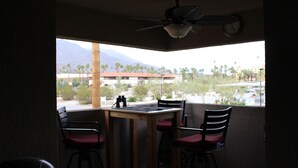 Un espace repas comprenant une table et des chaises, un ventilateur de plafond et une vue sur des palmiers et des immeubles.
