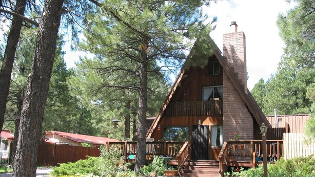 Une cabane en bois avec un toit à forte pente, une cheminée et une véranda dotée de balustrades en bois.