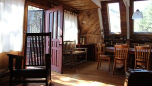 L’intérieur d’un chalet rustique, avec des murs et des planchers en bois, une porte rose, ainsi que plusieurs chaises et tables en bois.