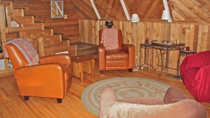 Une pièce chaleureuse de style loft, avec des murs en bois et un plafond en pente. Elle comprend un fauteuil en cuir, une petite table ronde avec une lampe et une chaise rouge.
