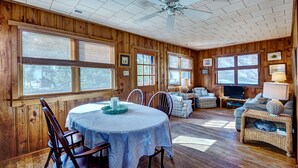 Interior de una cabaña de madera con una mesa de comedor, sillas, un sofá y un televisor.