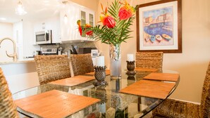 A dining area with a glass table, wicker chairs, and a vase with flowers. - SPECTACULAR BEACH CONDO. 2/2 PLUS DEN. HEATED POOL - EMAIL US. (Indian Shores)