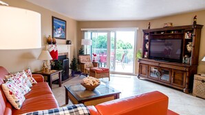 A living room with a sofa, a television, a fireplace, and a balcony with outdoor furniture. - SPECTACULAR BEACH CONDO. 2/2 PLUS DEN. HEATED POOL - EMAIL US. (Indian Shores)