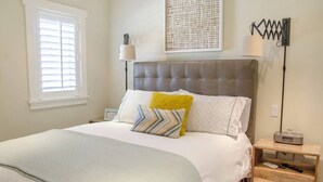 A bedroom with a large bed, a bedside table with a lamp, and a wall-mounted artwork. - Playa One Bedroom (251) (Carpinteria)