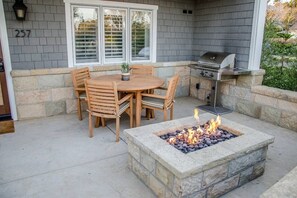 Un patio al aire libre con un hogar de piedra, una mesa y sillas de madera, y una parrilla.