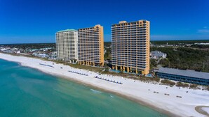 A beachfront hotel with multiple floors, a pool, and a beach area with umbrellas. - Corner Condo - Stunning Gulf Views -Comp. Beach Service, Water Park & Lazy River (Panama City Beach)