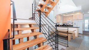 A modern staircase with wooden steps and metal railings leading to a kitchen area with wooden cabinets and a dining table. - Cool Coastal Tri-Level Condo with Ocean Views! (Newport Beach)