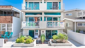 A two-story building with balconies, outdoor seating, and potted plants. - Cool Coastal Tri-Level Condo with Ocean Views! (Newport Beach)