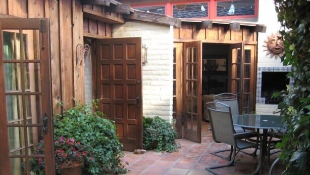 Un espacio al aire libre con una mesa y sillas, puertas de madera y plantas en macetas.