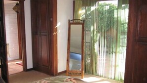 Un dormitorio con cama, un armario de madera, un espejo y una ventana con cortinas de bambú.