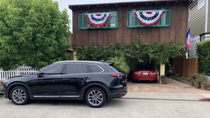 Un SUV negro estacionado frente a una casa con fachada de madera y marcos de ventanas verdes.