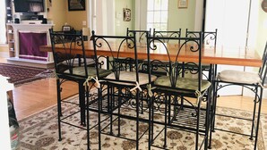 Un coin repas avec une table et des chaises en métal noir, un téléviseur placé au-dessus de la table et un tapis à motifs sur le sol.