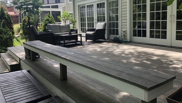Un patio couvert avec des meubles d’extérieur, une terrasse en bois et une maison blanche dotée de grandes fenêtres et d’une porte.