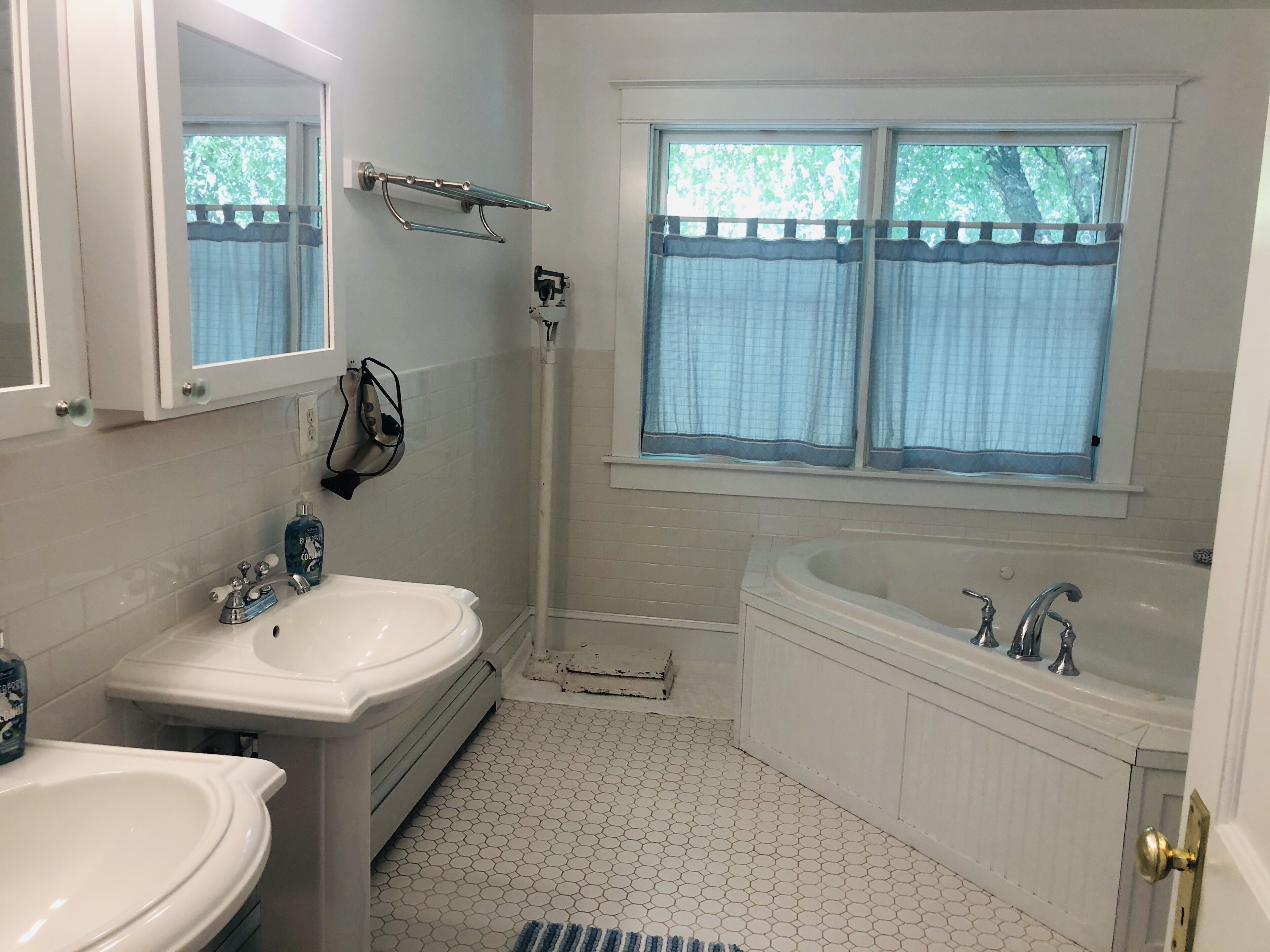 A bathroom with two sinks, a bathtub, a window with curtains, a shower, and a mirror.