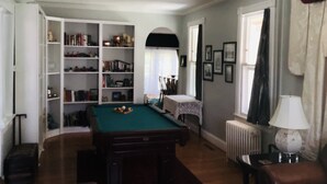Une pièce avec une table de billard, une bibliothèque et une fenêtre avec des rideaux.