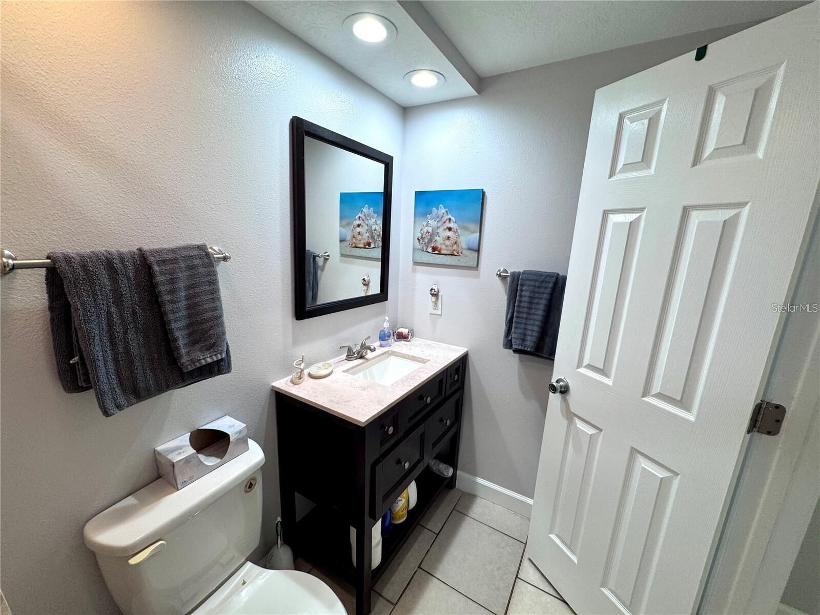 A bathroom with a toilet, sink, and mirror, featuring a towel rack and a door.
