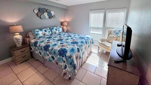 A bedroom with a bed, two bedside tables, a ceiling fan, decorative wall art, a window with blinds, and a television on a stand. - 5 minutes drive to nr Siesta Key  2BR/2BA condo Sienna Park. heated pool.. (Sarasota)
