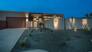 A modern house with a garage, a covered patio, and a landscaped garden with rocks and small plants. - PS Paradise: Contemporary Modern Home; Large with Modern Comforts (Palm Springs)