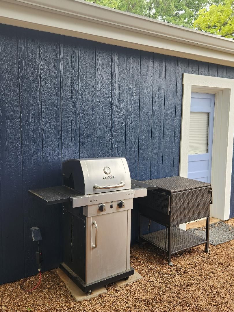 A barbecue grill with a side table, a power outlet, and a door in the background.