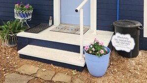 Une maison avec une porte bleue, un porche blanc, un paillasson, une poubelle et un panneau indiquant qu’il est interdit de fumer.