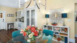 Une cuisine moderne avec des meubles blancs, une table à manger agrémentée d’un vase de fleurs et un élément décoratif mural.