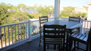 A covered outdoor area with a table and chairs, a white railing, and a view of trees and buildings. - Book now for 2026 (Orange Beach)