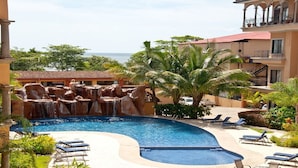 A pool with a waterfall feature, surrounded by lounge chairs and palm trees. - Two Story, 5 Bedroom Penthouse On Tamarindo Beach- New  (Tamarindo)