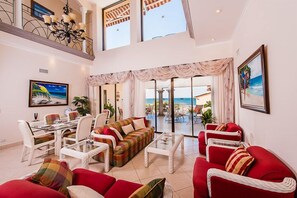 Amplia sala de estar con techo alto, comedor y vista al mar a través de puertas de vidrio grandes.