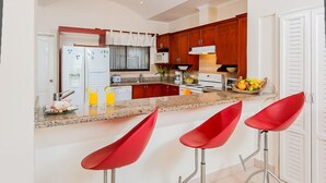 A modern kitchen with wooden cabinets, a granite countertop, and red bar stools. - Two Story, 5 Bedroom Penthouse On Tamarindo Beach- New  (Tamarindo)