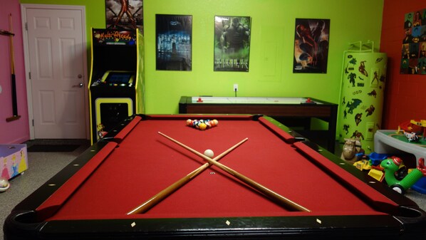 A pool table with a red felt surface, a cue stick, and billiard balls. - Princess, Pirate & Super Hero Rooms, Mickey Pool, Toys & Game Room For All Ages (Kissimmee)
