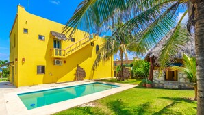 Un edificio amarillo con piscina, una escalera y una estructura de piedra con techo de paja.