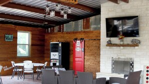 Un interior rústico con vigas de madera a la vista, chimenea de ladrillo y televisor montado en la pared.