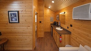 Interior de una cabaña de madera con kitchenette, un lavamanos, un espejo y un cuadro en la pared.