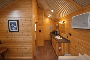 A wooden cabin interior with a kitchenette, a sink, a mirror, and a framed picture on the wall.