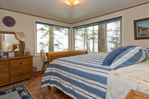 A bedroom with a large bed, a wooden dresser, a chair, and a window with a view of trees. - Beautiful Water Views & Private Beach Trail Between Sequim & PA (Port Angeles)