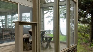 Ett takförsett utomhusområde med träbänkar och picknickbord, omgivet av glasväggar och ett trädäck.