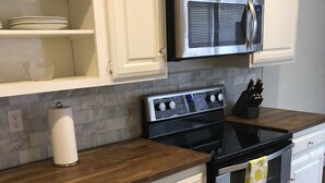 Une cuisine avec des meubles blancs, un four à micro-ondes en acier inoxydable, une cuisinière noire et un plan de travail en bois.