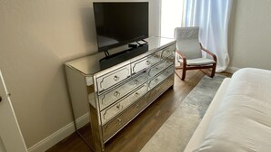 Une chambre d’hôtel avec un téléviseur à écran plat posé sur une commode à miroir, une chaise blanche et un grand lit.