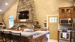 Una cocina con chimenea de piedra, armarios de madera, una isla grande con taburetes de bar y electrodomésticos modernos.