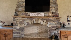 Una chimenea de piedra con un televisor de pantalla plana, armarios de madera y un ventilador de techo en una sala de estar.