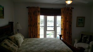 A bedroom with a bed, a chair, a lamp, and a window with curtains. - Beautifully decorated townhome just steps from the beach & Lighthouse (Tybee Island)
