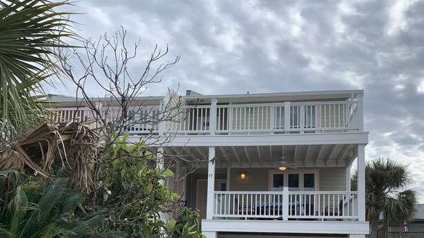 A two-story building with a balcony on the upper floor, a garage entrance, and a sign for Tybee Island Vacation Rentals. - Beautifully decorated townhome just steps from the beach & Lighthouse (Tybee Island)